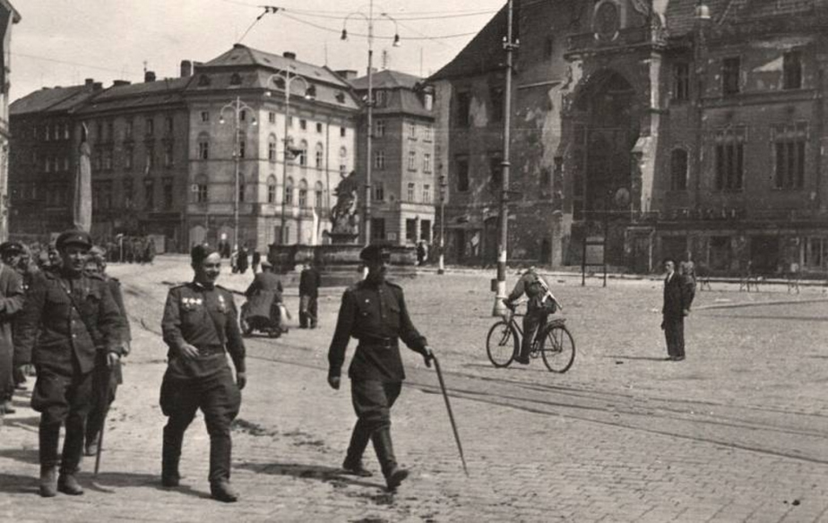 Sovětští vojáci pochodují po Horním náměstí v Olomouci kolem poničené radnice. 